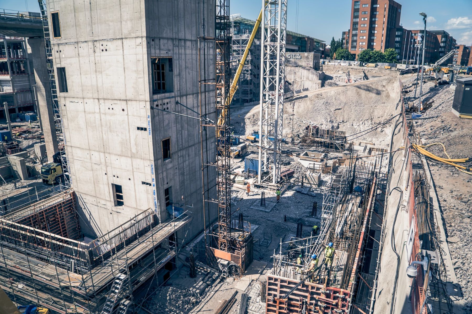 Aerial view of a concrete frame structure at a construction site, with a crane lowering material into an excavation